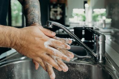 Close up of a man with a tattooed arm washing hands with soap in a sink