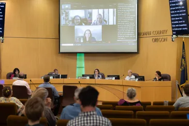 Audience members, Board of Commissioners and virtual presenters attend a meeting in the boardroom. 