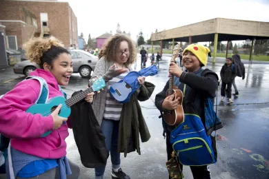 Three SUN School participants smiling and playing their ukuleles