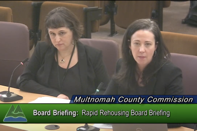 Lori Kelley and Anna Plumb from the Joint Office sit at the dais in the Multnomah County boardroom