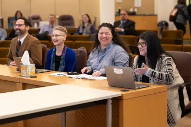 Four people sit at a table presenters table for board briefing