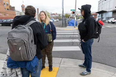 Two MHAAO staff members face and talk with an unidentified individual wearing a backpack and carrying a blanket, whose back is facing the camera