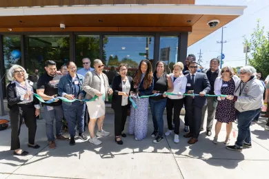 A large group of County and community leaders cut a blue ribbon in front of a new Community Health Center.