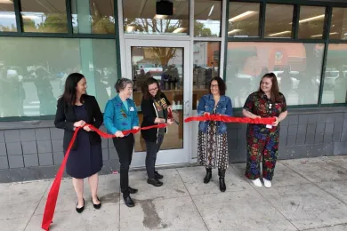 Anna Plumb, Mary Nolan, Jessica Vega Pederson and Do Good Multnomah Staff cut a ribbon in front of a building.