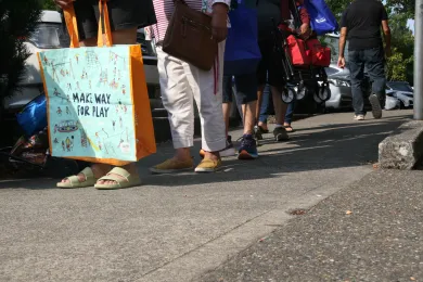  A ground-level, eye-level shot of a queue of people on a sidewalk.