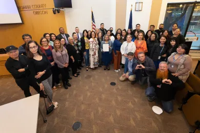 County staff and community members stand with the Board of County Commissioners in a boardroom with the signed proclamation. 