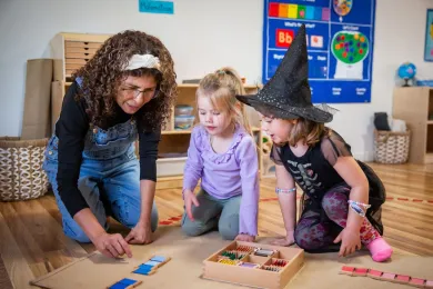 A teacher and two students play on the floor at Magic Shapes Preschool