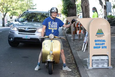 voter on moped returns ballot at drive up official ballot drop site location
