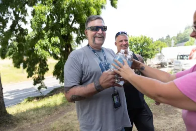 Outreach workers hand water bottles to a person out of frame.