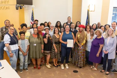 A large group of people smile for a photo at a Multnomah County Juneteenth Proclamation ceremony, with Commissioner Shannon Singleton in the center holding the framed document.