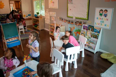 Several preschool children sit at tables working on projects in their classroom.