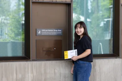 A voter holds a ballot return envelope next to an Official Multnomah County Ballot Drop Site at the East County Library. 