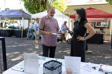 Ellen DeJoy, right, from the Office of Community Involvement, speaks with a community member at the Kenton farmer's market about openings on the County's Charter Review Committee.