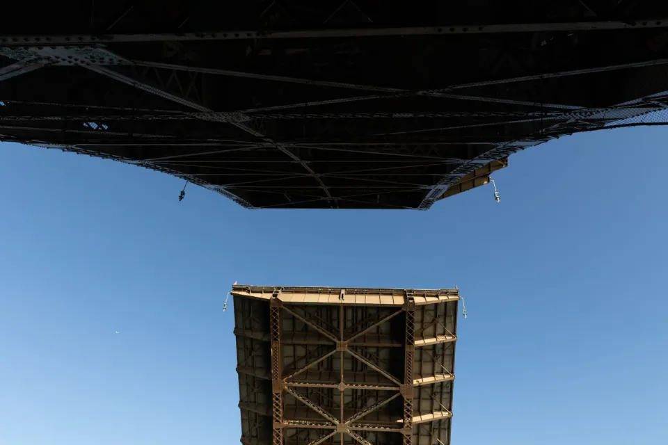A view looking up from beneath a bridge as the two lift spans open up, with a bright blue sky above.