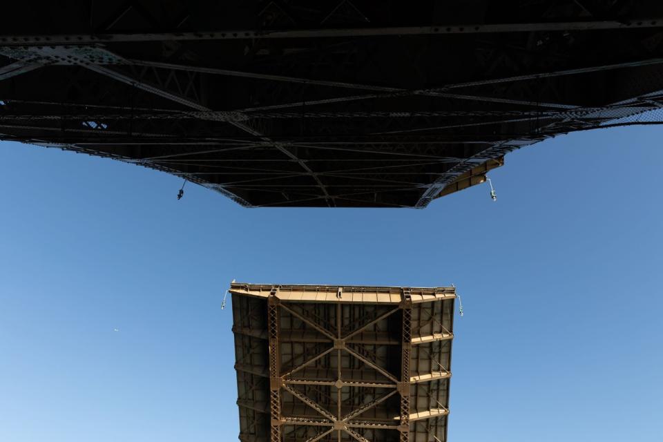A view looking up from beneath a bridge as the two lift spans open up, with a bright blue sky above.