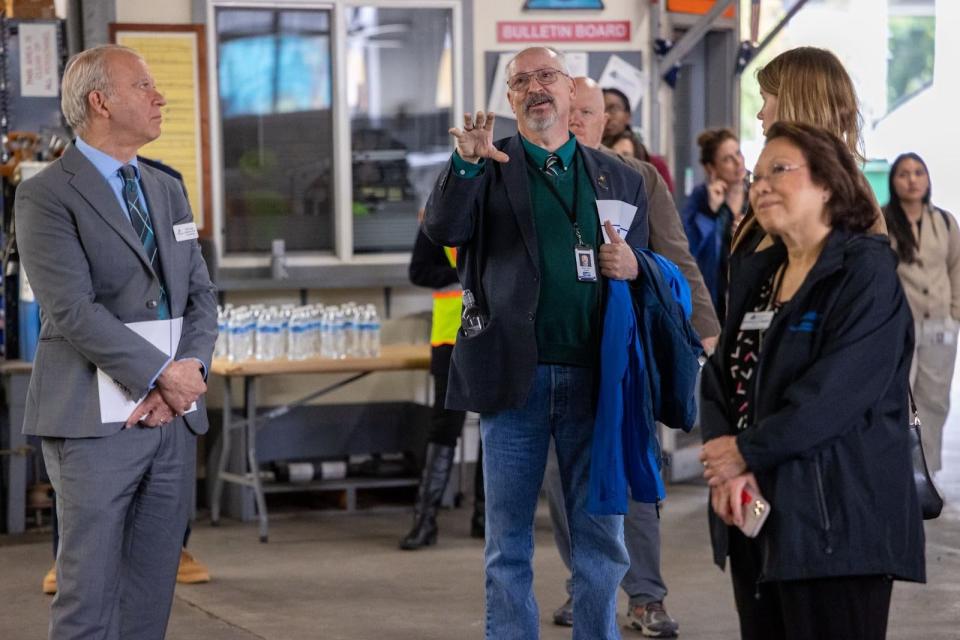 A man standing in a large garage gestures as he asks a question of a speaker.