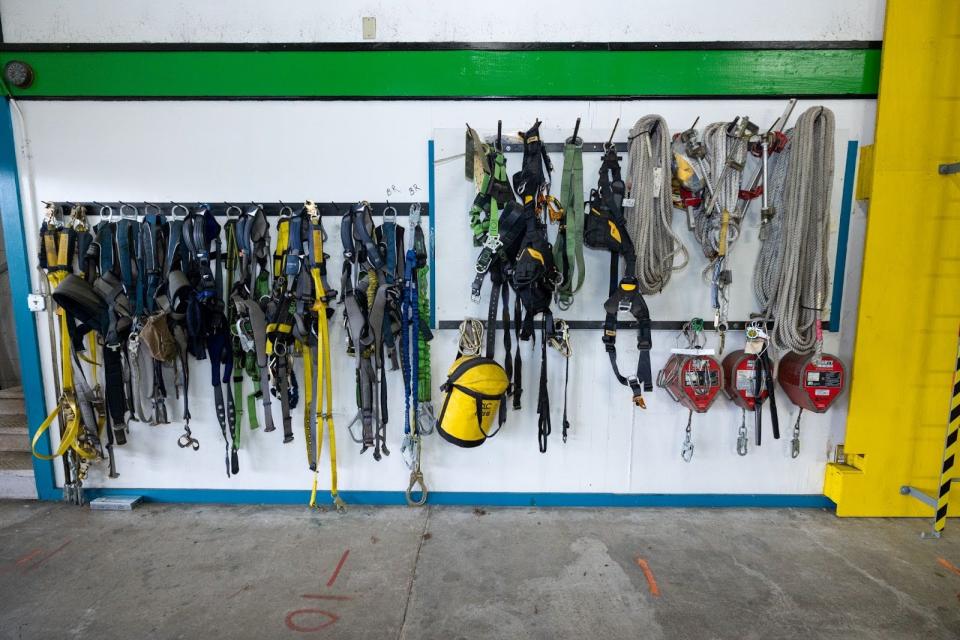 A variety of ropes, climbing harnesses and other gear hung on racks mounted on a wall.