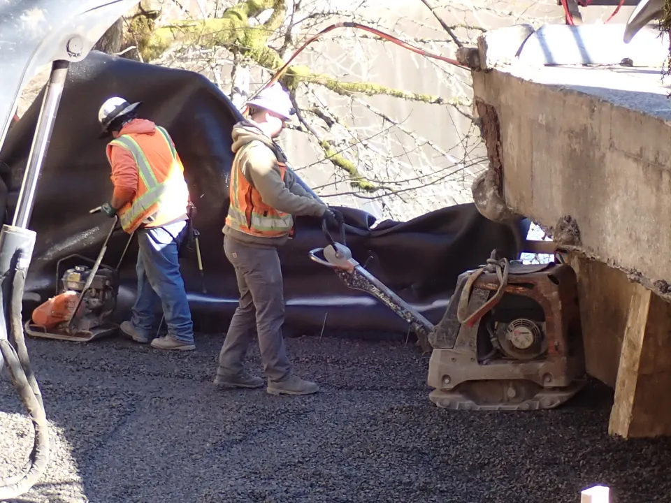 A crew using machinery to compact gravel near the end of the bridge.