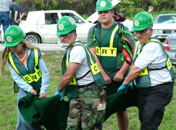 Volunteers wearing hard hats and vests practice carrying a fake victim