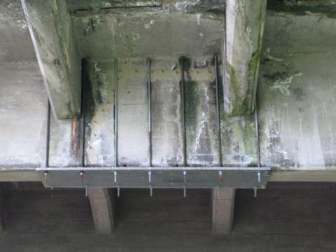 A steel plate and rods attached to the deteriorating concrete on the underside of the bridge.