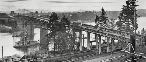 The partially constructed sellwood Bridge, with cranes and scaffolding mounted on work barges in the river.