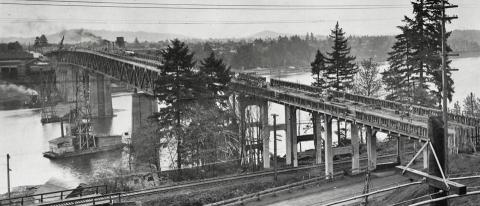 The partially constructed sellwood Bridge, with cranes and scaffolding mounted on work barges in the river.