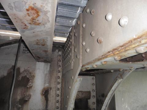 A view of structural steel members on the underside of a bridge. Their paint is peeling in spots, and rust and corrosion can be seen.