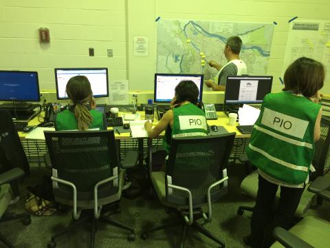 PIOs in green vests working on computers and on the phone