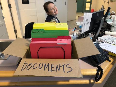 A worker in the EOC making a funny face behind a big box labeled Documents