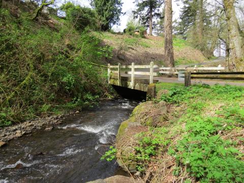 A side view of a small wooden bridge with a white wooden fence over a creek.