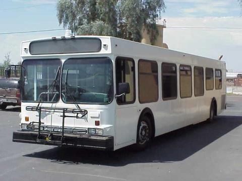 A white-painted bus with a bike rack on front, sitting in a parking lot.