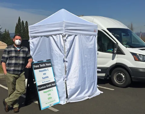 health worker standing next to a clinic van and privacy tent in a parking lot