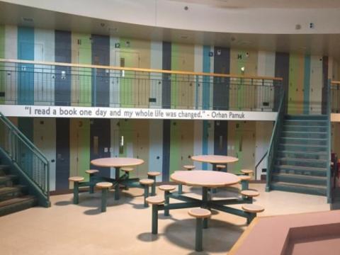 Image of a common area at the Donald E. Long Juvenile Detention Facility. There is a quote painted on the balcony that says, "'I read a book and one day my whole life was changed.' - Orhan Farmuk"
