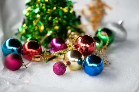 Table centerpiece at Appreciation Day at Bienestar 12/10/2021: background is blurry with bright color -it's possibly tinsel. In the foreground are red, gold, blue, green and fuschia class balls, interlaced with gold beads.