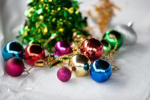 Table centerpiece at Appreciation Day at Bienestar  12/10/2021: background is blurry with bright color -it's possibly tinsel. In the foreground are red, gold, blue, green and fuschia class balls, interlaced with gold beads.