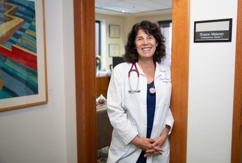 Commissioner Sharon Meieran standing in the oak doorway of her office wearing her white doctor's coat and stethoscope. 