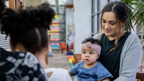 a young woman holding a baby on her lap listens to a friend