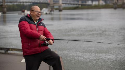 Happy Asian man in a red jacket fishing off a dock in the Willamette River