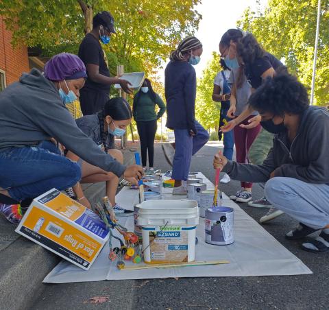 youth of color gather around a tarp to mix paint for a street mural