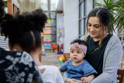 Mother holding her child on her lap talking with friend