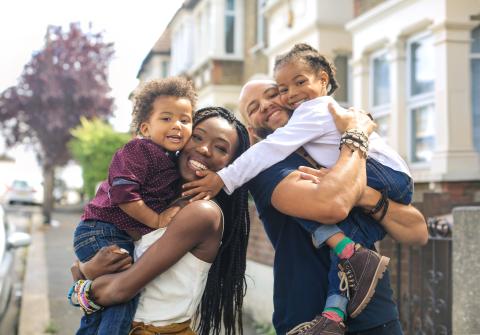 Happy family with two kids stands outside their apartment.