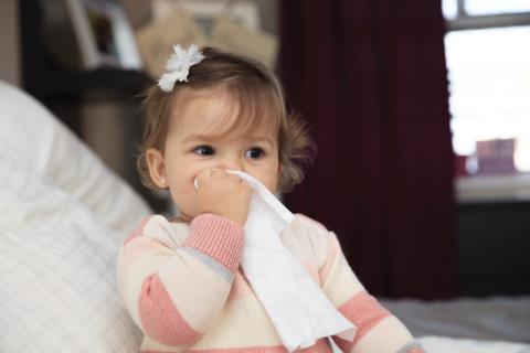 baby girl sitting up in bed, holding a tissue to her nose