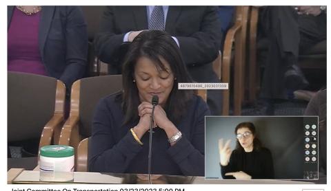 Photo of Multnomah County Commissioner Susheela Jayapal seated at a table in front of a microphone, with an inset image of a sign language interpreter.