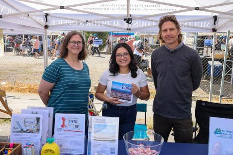 three people tabling a street fair with the middle person holding a resource guide book