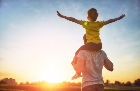 Child on parent's shoulders during sunset