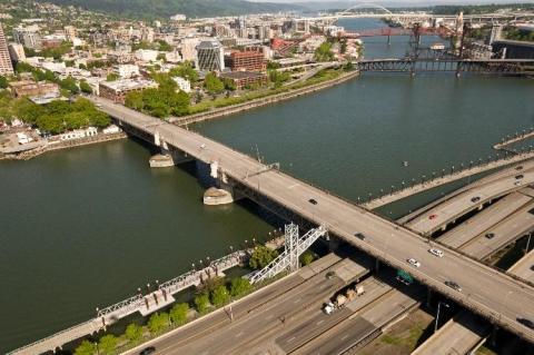 An aerial view of the Burnside Bridge, showing I5 in the foreground, and downtown Portland and the Steel, Broadway and Fremont bridges in the background.