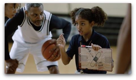 Basketball players huddle around Black girl holding up a tactic board that shows a syringe and bandage, and the message Find Your Shot.
