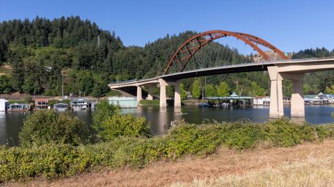 The Sauvie Island Bridge, seen from the Sauvie Island side, with houseboats on the far side of the Multnomah Channel and forested hills in the background.