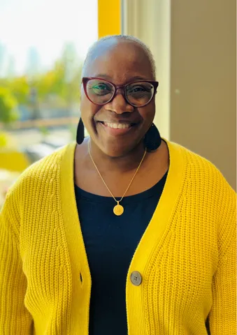 woman in black top with yellow seater and glasses.