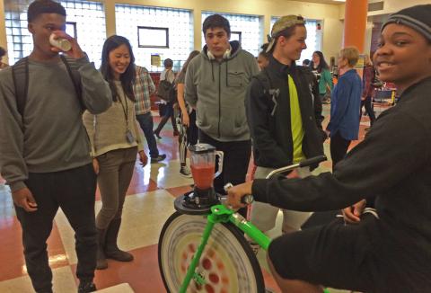 students gathered around a stationery bike being used to power a blender